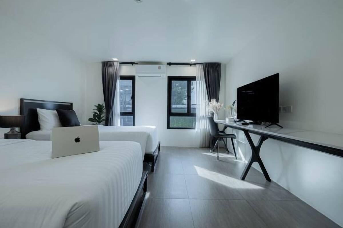 Habitación de hotel con dos camas, un escritorio con una computadora portátil, un televisor de pantalla plana y un amplio ventanal con cortinas.