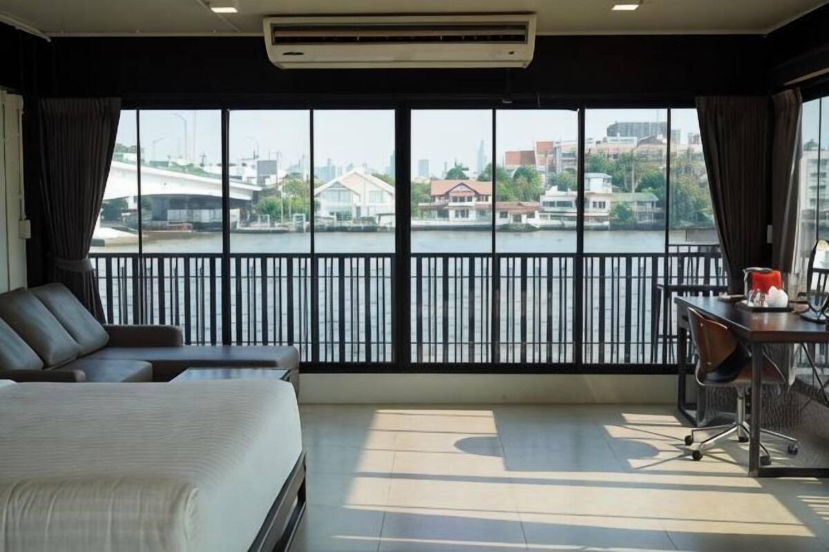 Habitación de hotel con cama, escritorio y vistas a un paisaje urbano a través de amplios ventanales.