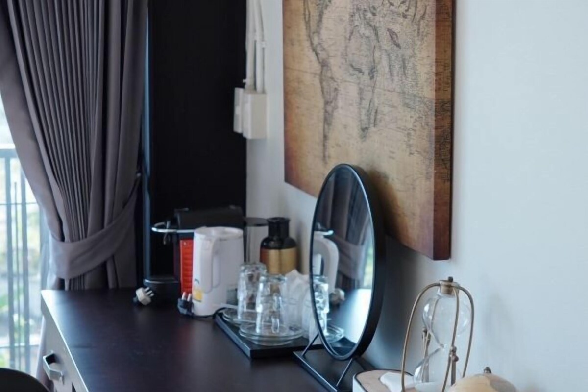 A hotel room with a dark wooden desk, a coffee maker, a glass carafe, a mirror, and a map on the wall.