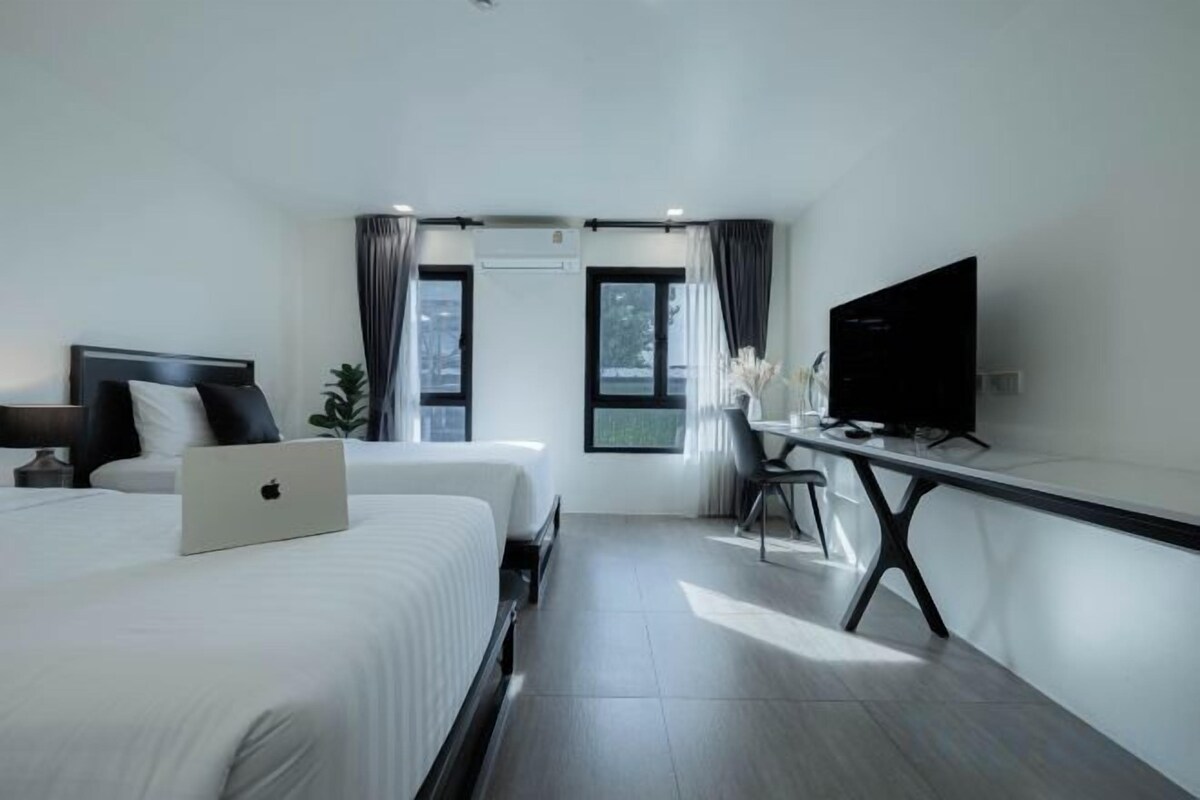 A modern hotel room with two beds, a desk, a flat-screen TV, and a laptop.