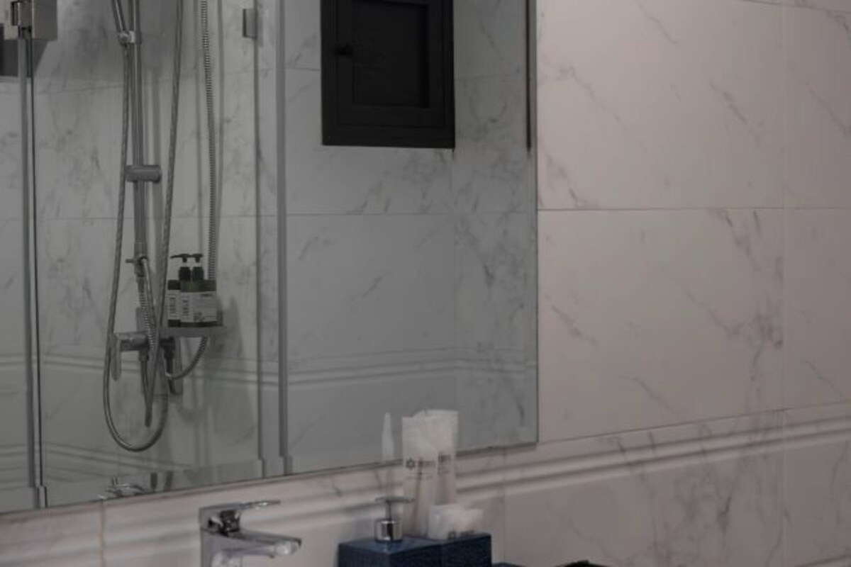 A bathroom with a shower, a mirror, and a towel dispenser.