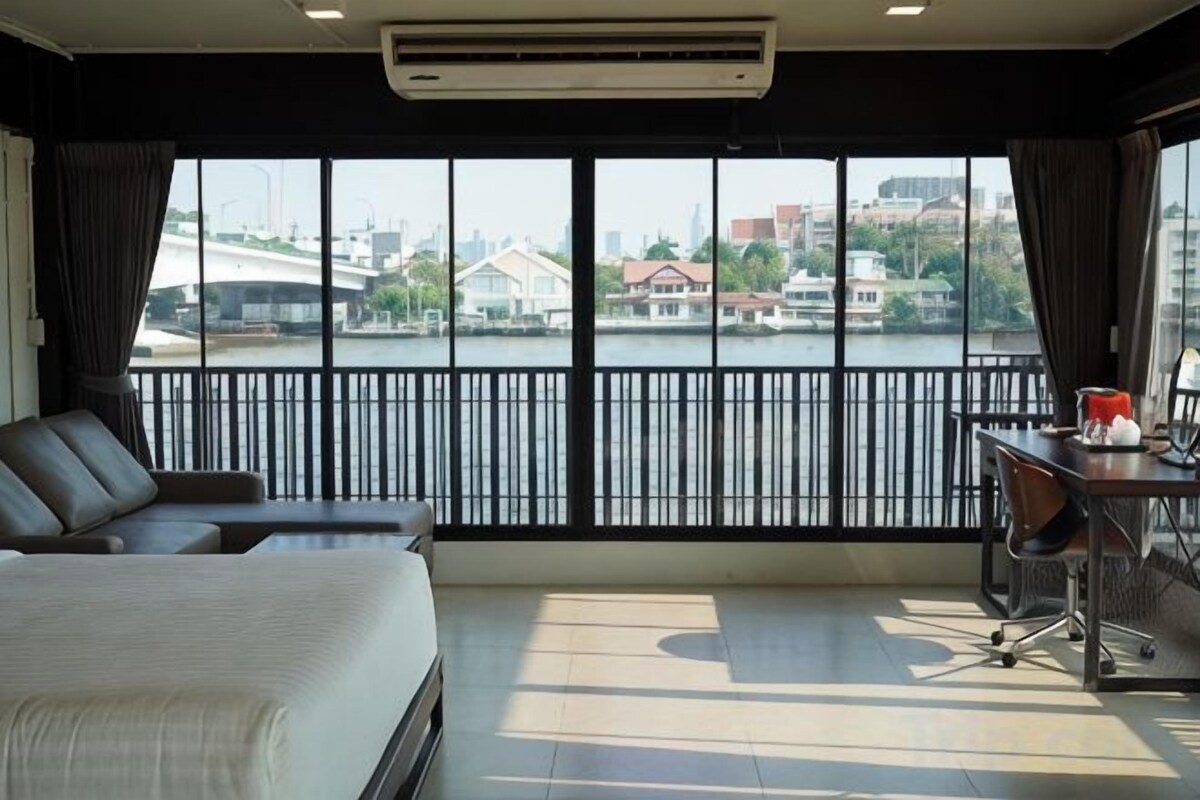 A hotel room with a bed, a desk, and a view of a river and buildings.