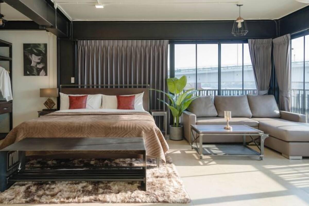 Habitación de hotel moderna con una cama grande, un sofá, una mesa de centro y vistas de la ciudad a través de amplias ventanas.