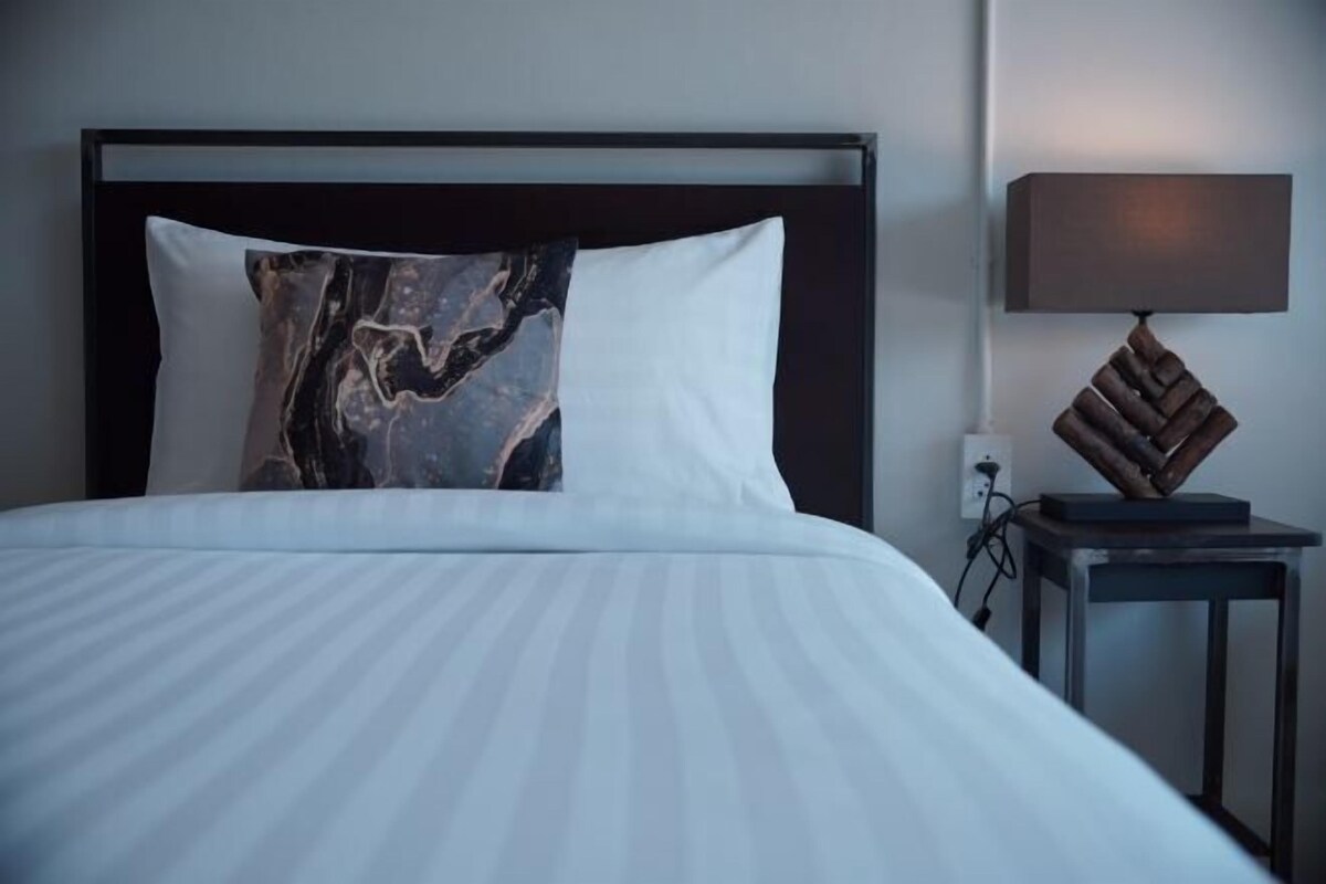 A neatly made bed with a marble-patterned pillow, a plain white pillow, and a small table with a lamp beside it.