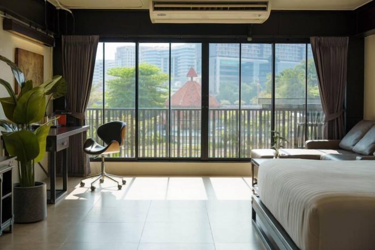 Una habitación de hotel moderna con un gran ventanal, un escritorio con silla, una cama y una planta en maceta.