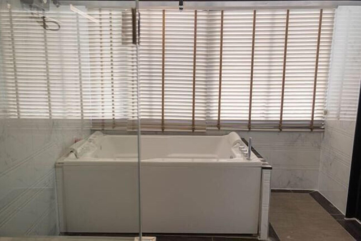A bathroom with a bathtub, a glass shower enclosure, and a window with blinds.