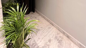 Un pasillo estrecho con una cortina oscura, una planta en maceta y un piso de mármol.