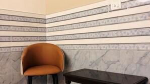 Une pièce d’angle avec un fauteuil marron et une petite table en bois, le tout adossé à un mur orné de carreaux décoratifs et de marbre.