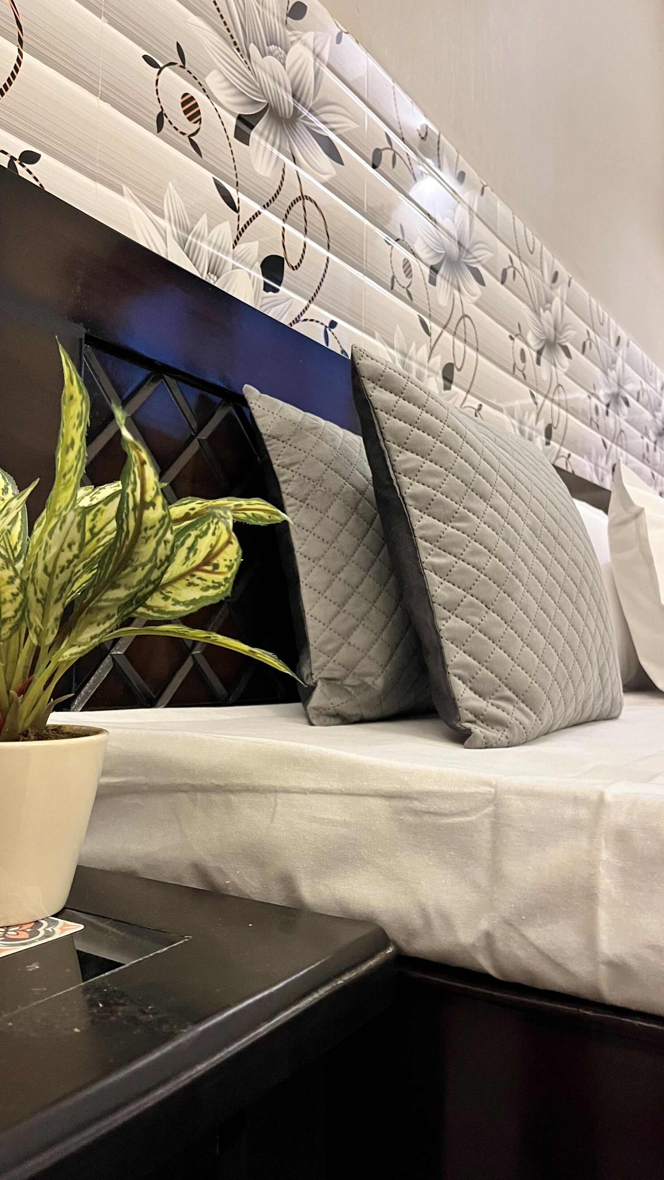 Una cama con cabecera de estampado floral, almohada acolchada y una planta en maceta sobre una mesita de noche.