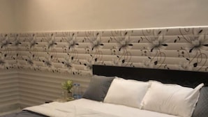 Una cama con un edredón oscuro, un cabecero con estampado floral y una mesita de noche con una planta.