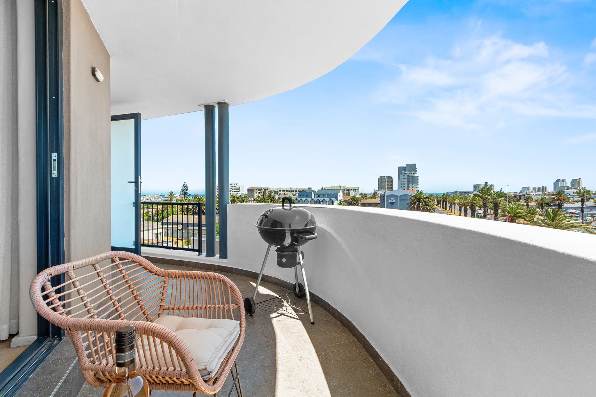 Ein Balkon mit Korbmöbeln, einem Grill und Blick auf die Stadt.
