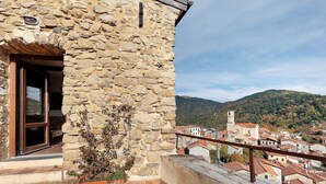 Un edificio de piedra con un balcón, una ventana y vistas a un pueblo y colinas.