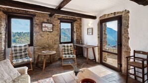 Una habitación rústica con paredes de piedra, vigas de madera, vistas a la montaña y una zona de estar acogedora con una mesa y sillas.