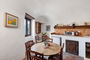 Una cucina con un tavolo rotondo in legno, sedie, un forno a microonde e una piccola finestra.