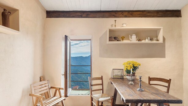 A rustic dining area with a wooden table, chairs, and a view through a window.