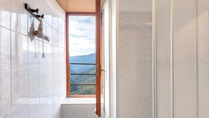 A bathroom with a shower, a window with a view of mountains, and a tiled wall.