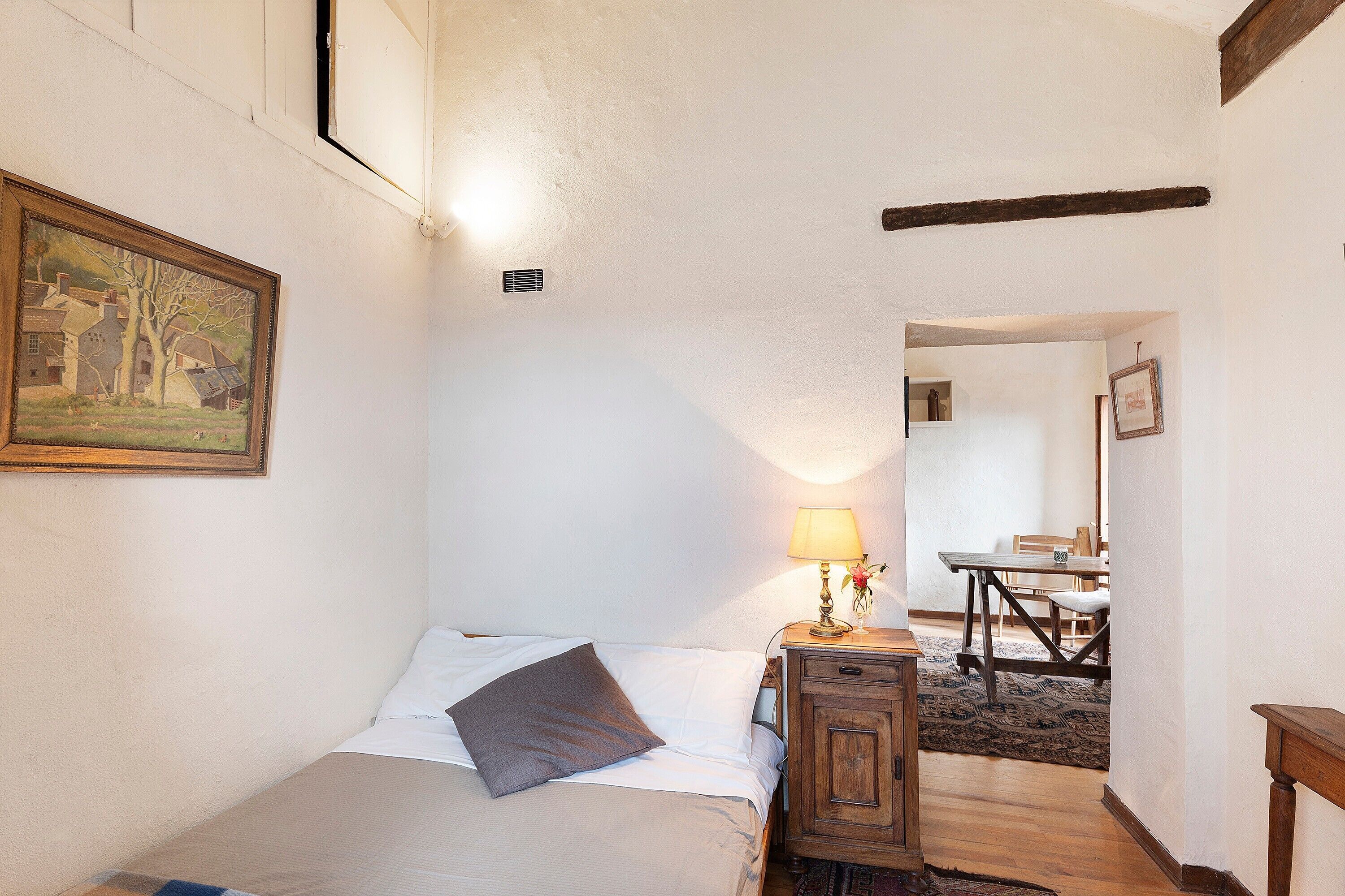 Ein Schlafzimmer mit einem Bett, einem Nachttisch mit Lampe, einem Bild an der Wand und Holzboden.