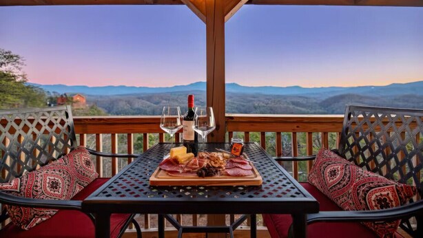 Un espacio de estar al aire libre cubierto con una mesa dispuesta para una comida, que incluye una botella de vino, copas y una variedad de carnes.