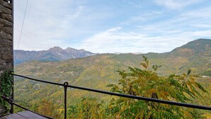 Blick auf Berge vom Balkon mit Geländer, Steinmauer und Holztisch.