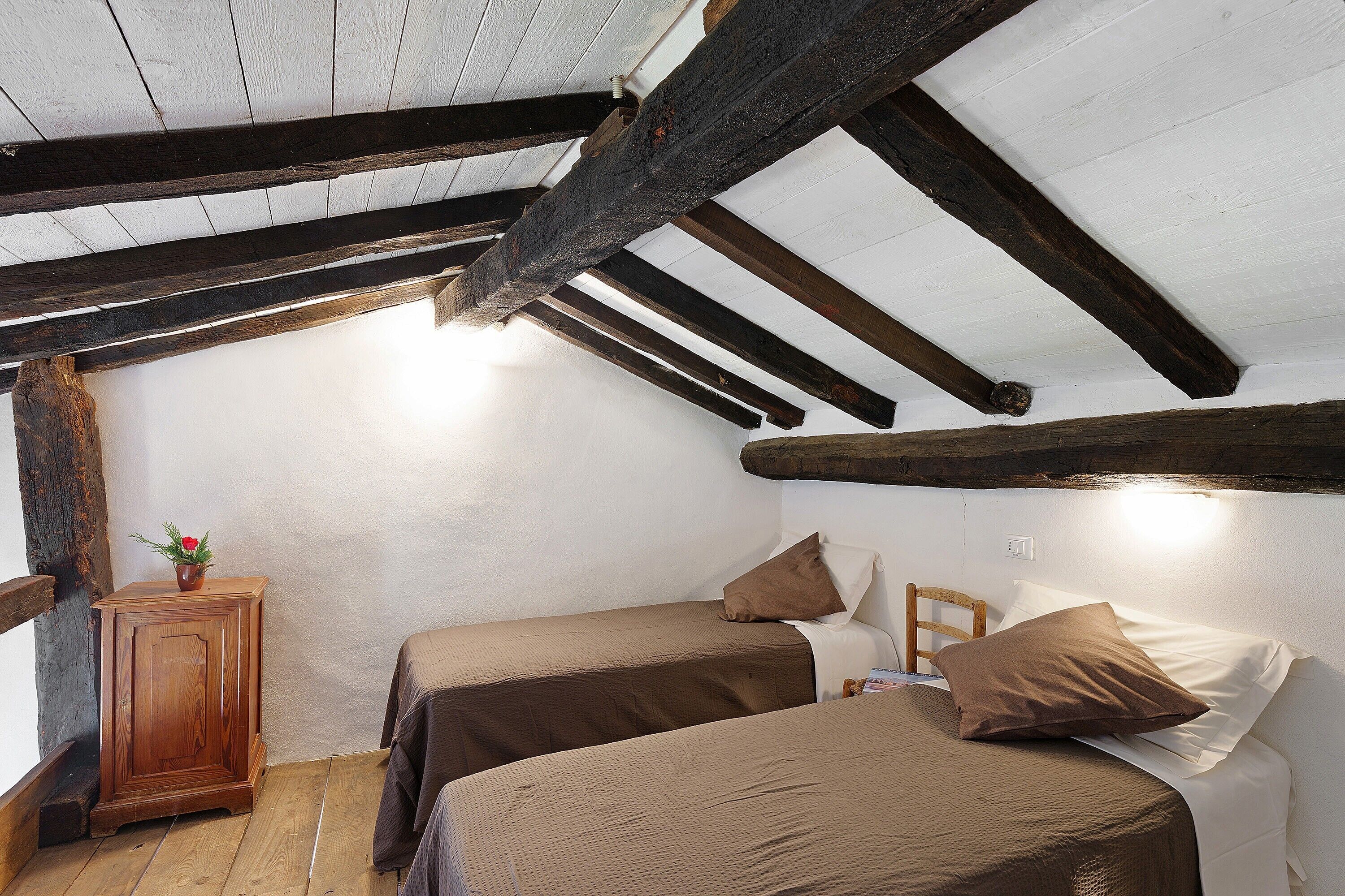 Une chambre avec deux lits, des poutres apparentes, une petite armoire et une fenêtre.