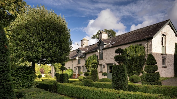 A traditional stone building with a symmetrical garden layout, featuring neatly trimmed hedges and topiary. - West Cottage (Llandovery)