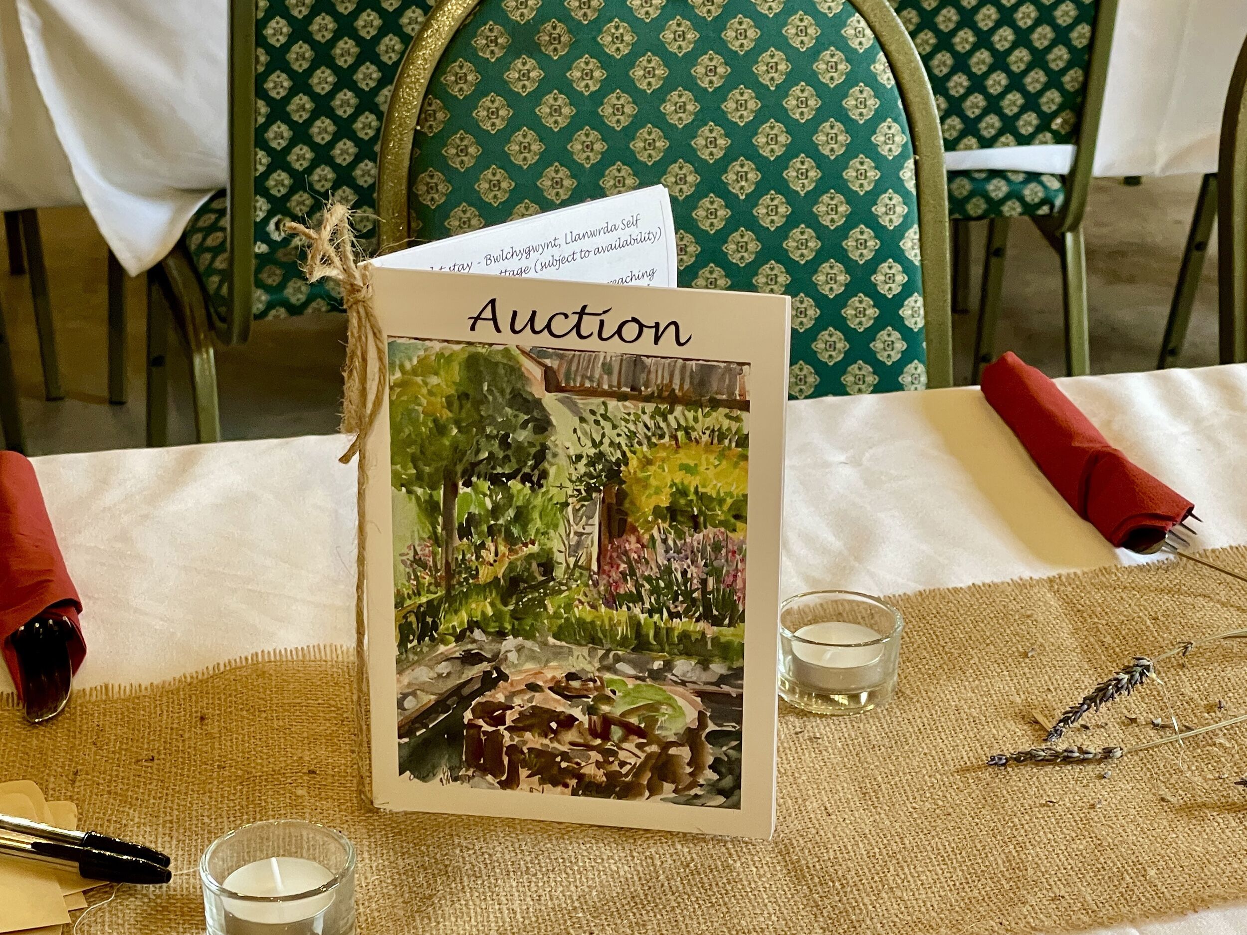 A table with a card labeled "Auction" featuring a painting of a garden scene.