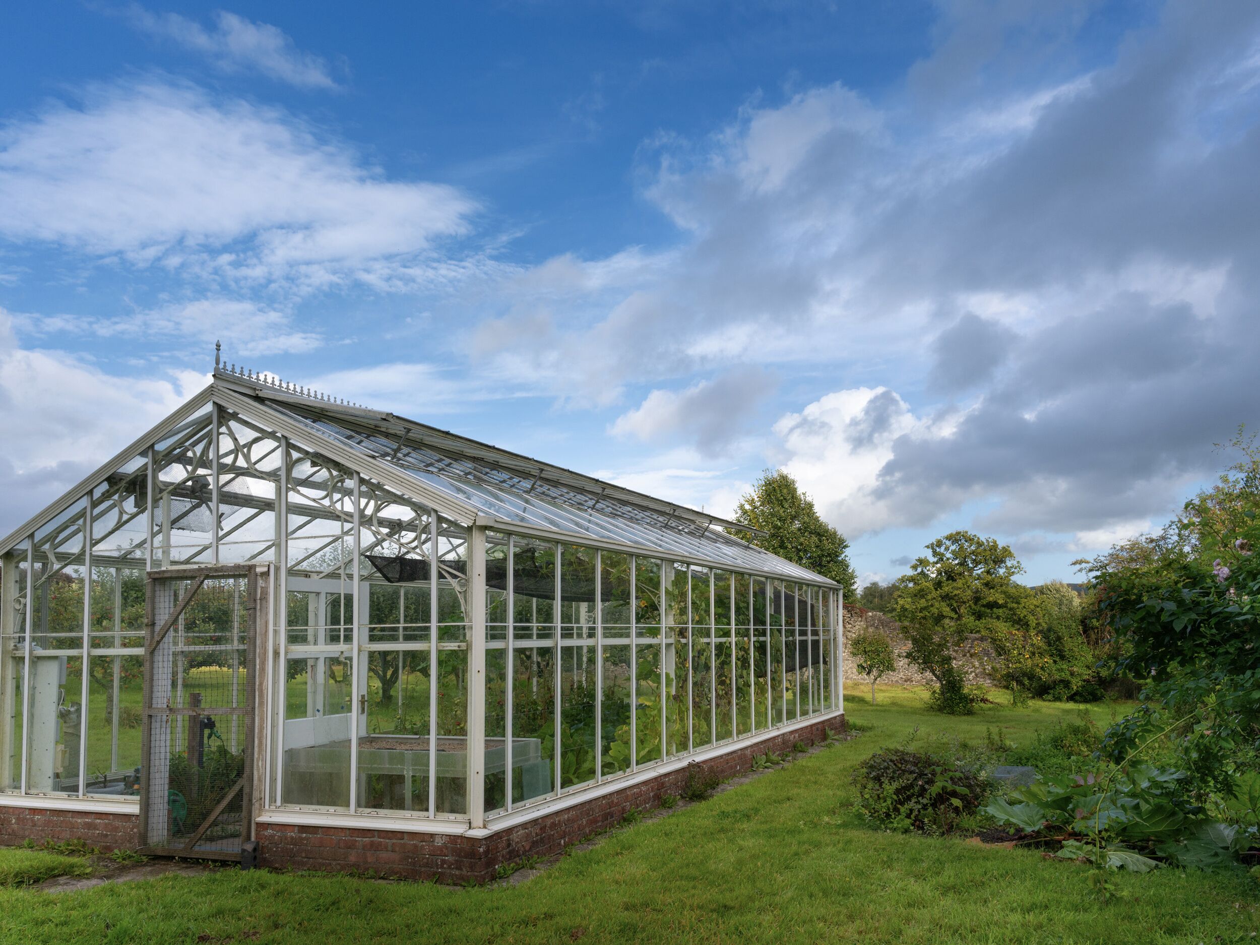 A large greenhouse with a glass roof and walls, surrounded by a grassy area and trees.