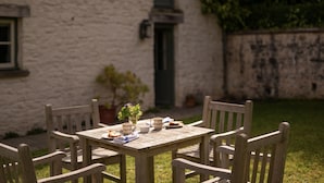 A wooden table with chairs, a vase with flowers, and a plate of food. - West Cottage (Llandovery)