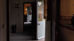 A hallway with a white door leading to a room with a window, a wooden cabinet, and a wall-mounted light fixture. - West Cottage (Llandovery)