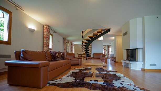 A spacious living room with a brown leather sofa, a wooden coffee table, and a large cowhide rug. A spiral staircase leads to an upper level. - Duplex apartment, sleeps 10, nature view (Giez)