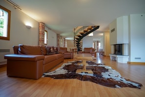A spacious living room with a brown leather sofa, a wooden coffee table, and a large cowhide rug. A spiral staircase leads to an upper level.