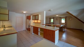 A spacious kitchen with wooden cabinets and a central island, a dining area with a table and chairs, and a view of the outdoors through a window. - Duplex apartment, sleeps 10, nature view (Giez)