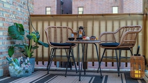 Een balkon met twee rieten stoelen, een kleine tafel, een bloempot en een lantaarn.