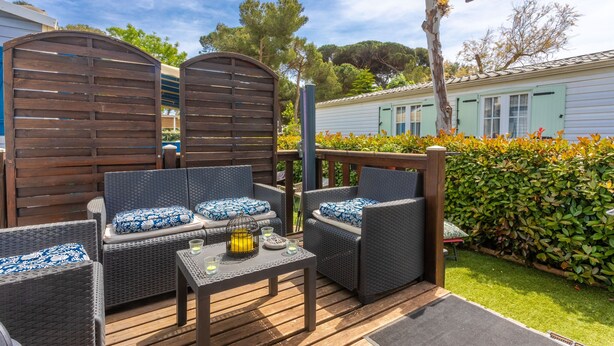 A patio area with wicker furniture, a table with drinks, and a view of a house in the background. - Mobile Home for 6 with Private Terrace, Wi-Fi & Air Conditioning in Hyères (Hyères)