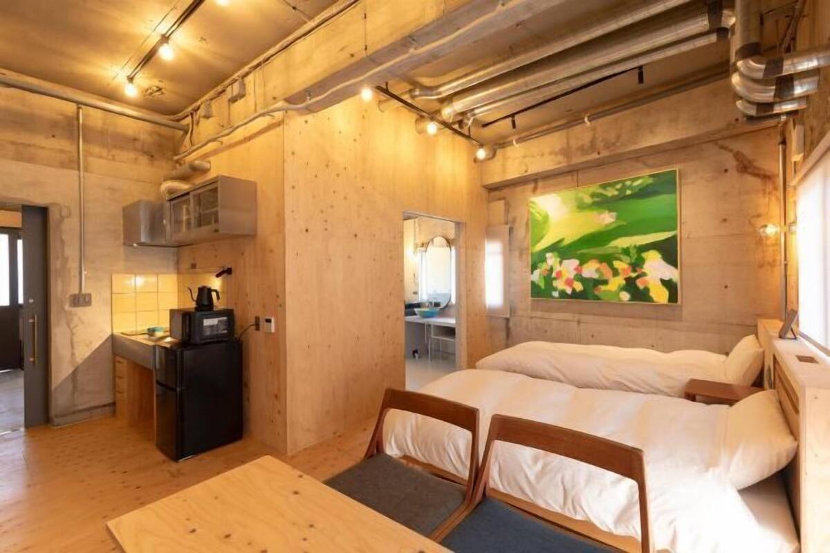 A compact room with a bed, a small kitchenette, and a painting on the wall.