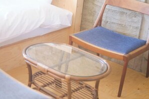 A bed with white bedding, a wooden chair with a blue cushion, and a glass table. - HAJIMARI Beppu (Beppu)