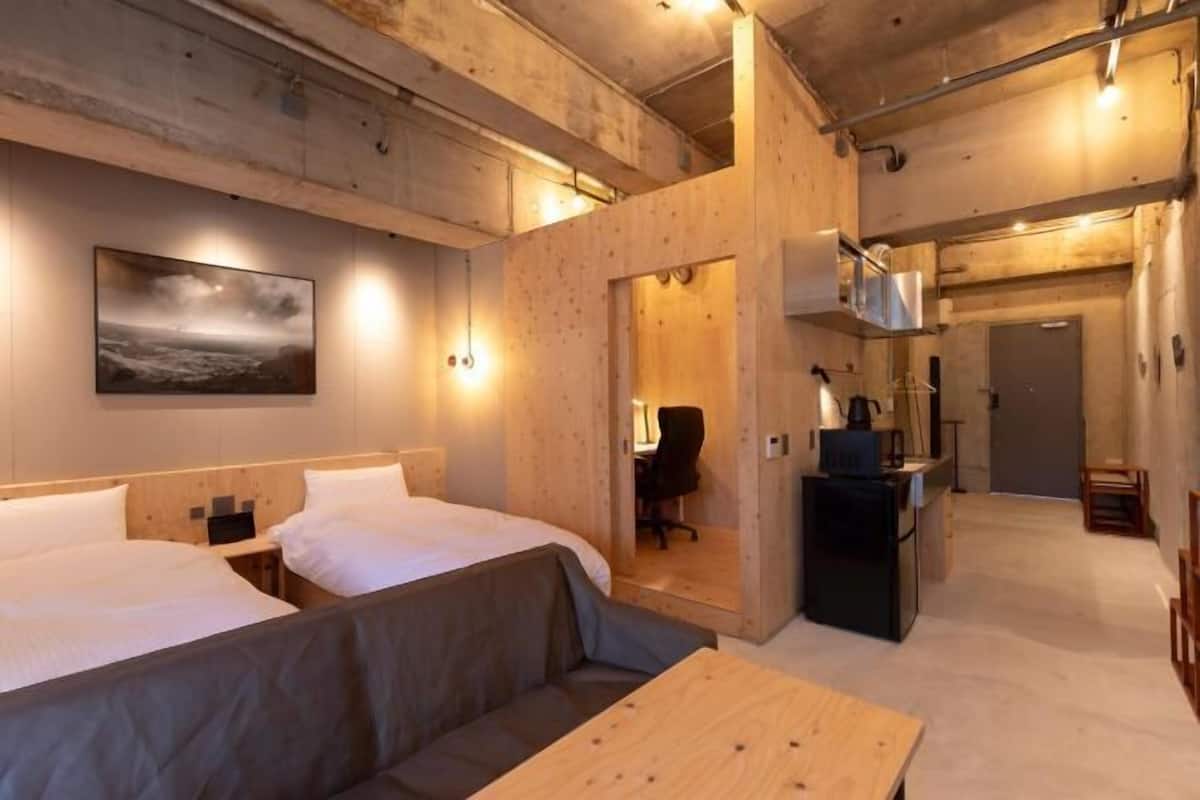 A hotel room with two beds, a sofa, a wooden table, a kitchen area, and a painting on the wall.