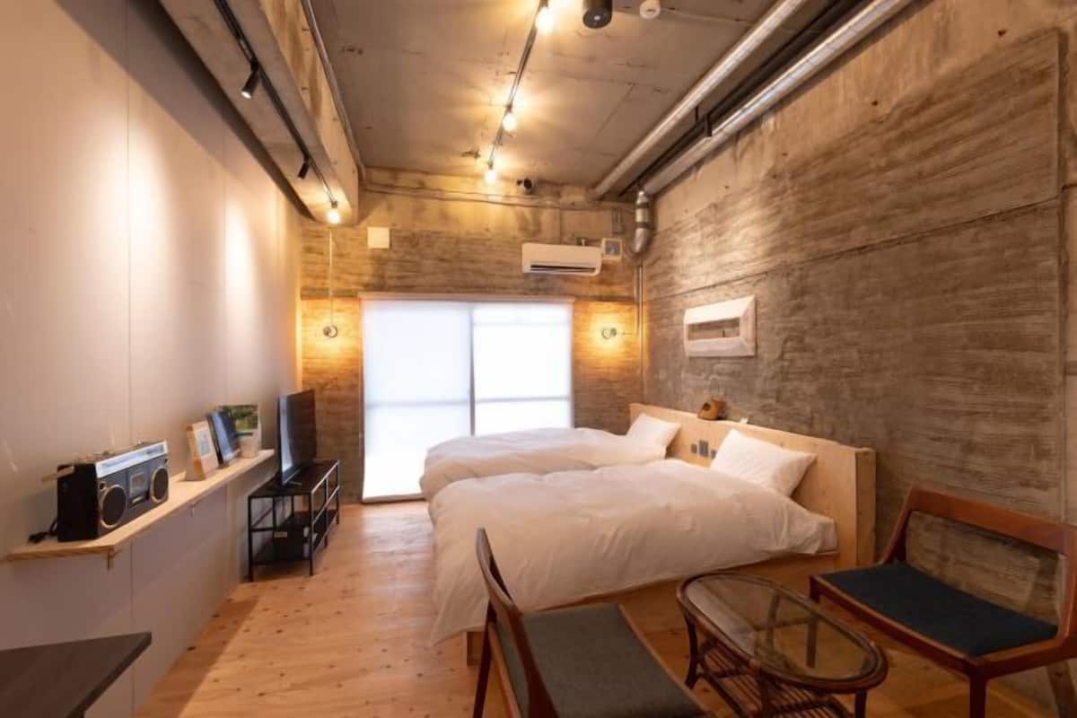 A bedroom with a wooden wall, a bed, a TV, a radio, and a window.