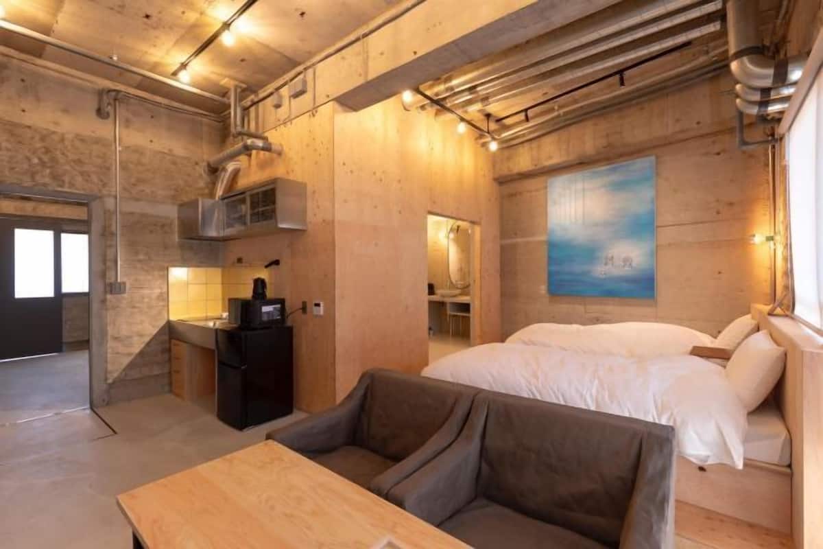 A modern hotel room with a wooden interior, a bed, a sofa, a table, and a painting on the wall.