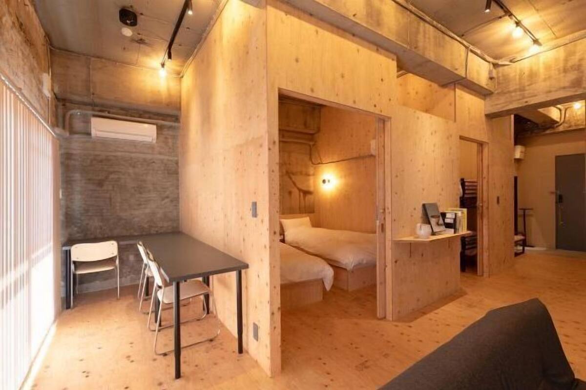A compact room with a bed, a desk, and a chair, featuring wooden walls and a ceiling with exposed beams.