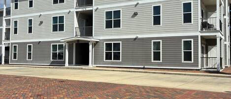 A multi-story residential building with a brick-paved entrance area and a clear blue sky.