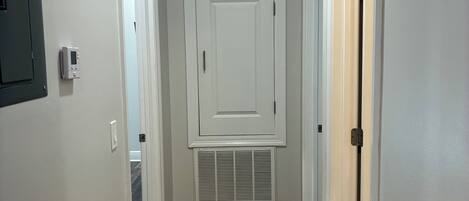 Un pasillo con suelo de madera, paredes blancas y una puerta central con respiradero.