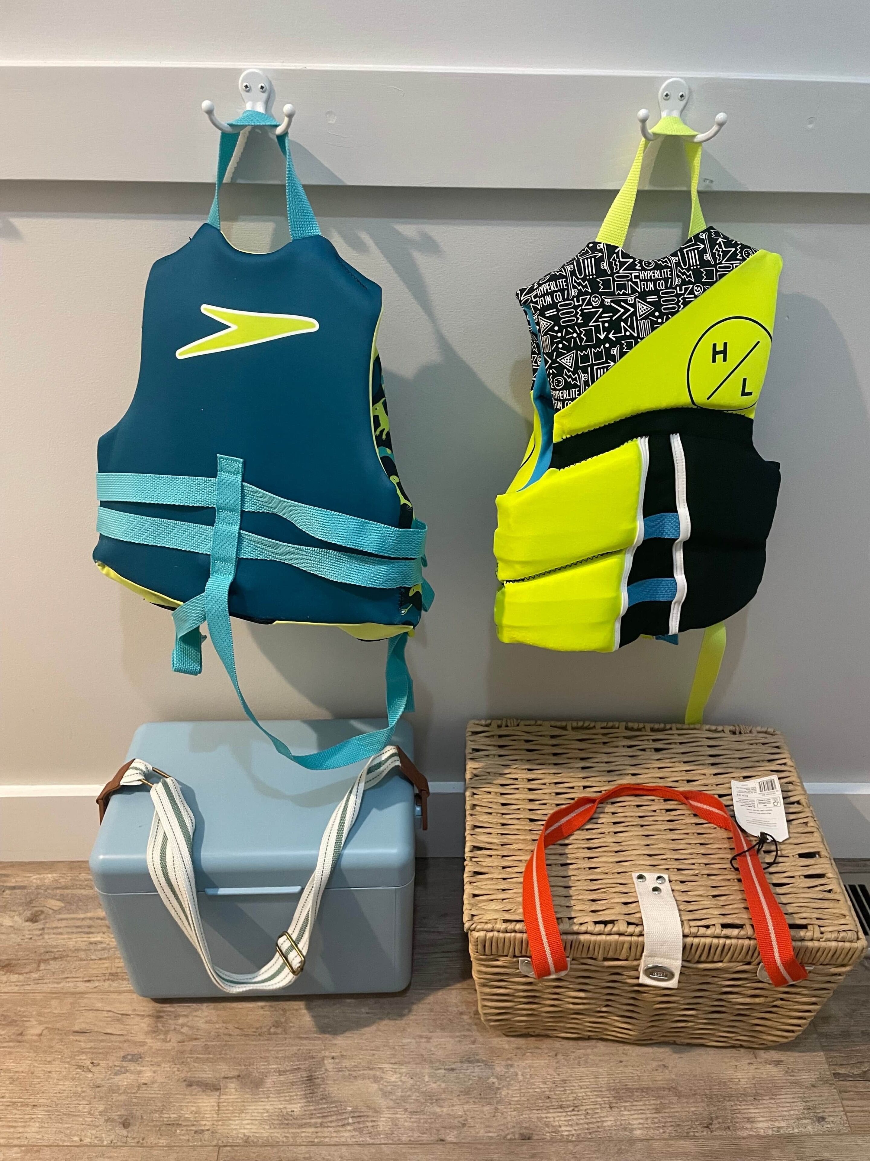 Two swimwear items hanging on a wall, a grey suitcase, and a wicker basket with a red strap.