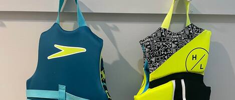 Two swimwear items hanging on a wall, a grey suitcase, and a wicker basket with a red strap.