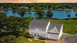 A large, single-story house with a garage, surrounded by a well-maintained lawn and trees, with a lake in the background.