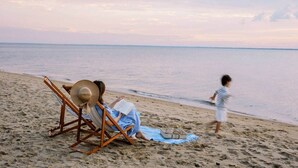 A beach scene with a wooden chair and a hat, a person reading a book, and a child running.