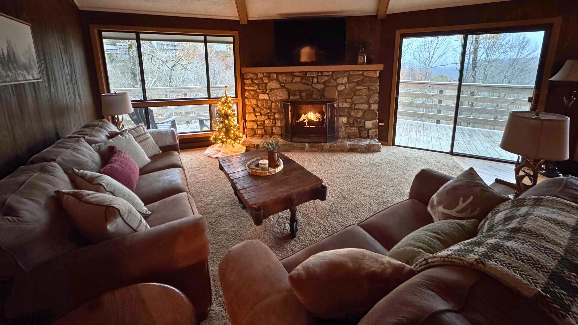 A cozy living room with a stone fireplace, leather sofas, and a Christmas tree.