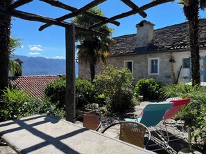 A stone building with a tiled roof, outdoor seating area with chairs, and a view of mountains. - Casa del Prete (Cannero Riviera)
