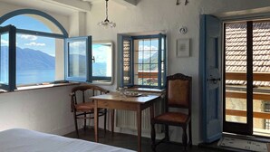 A room with a bed, a wooden table, two chairs, and a view of mountains through open windows. - Casa del Prete (Cannero Riviera)