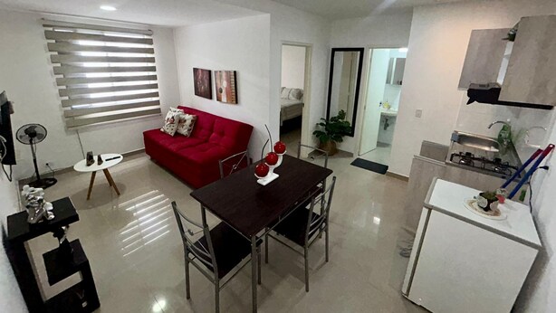 A modern living room with a red sofa, a dining table with chairs, a small white table, and a kitchen area with a refrigerator and sink. - Apartamento loft cali (Cali)